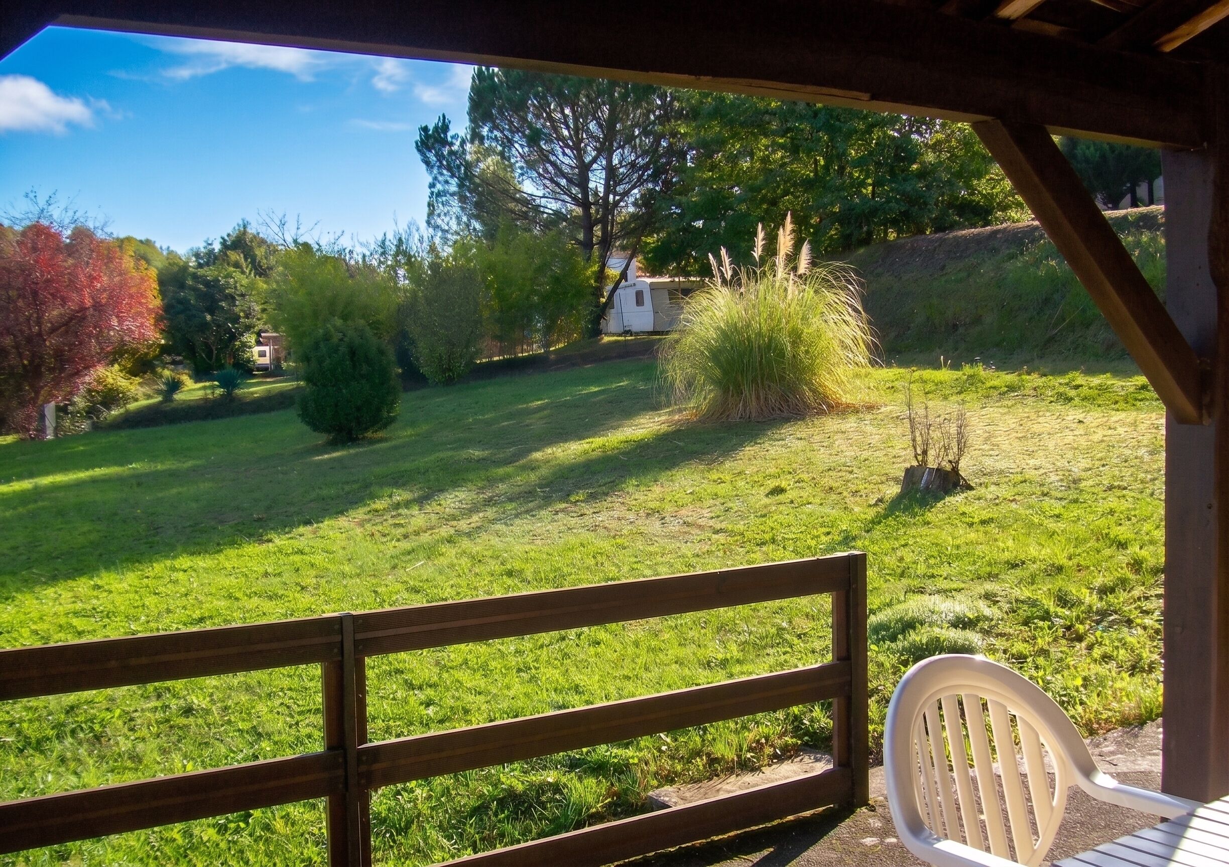 Une terrasse en bois avec une chaise blanche, une pelouse verdoyante et une maison en arrière-plan.
