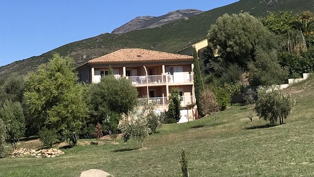 A two-story house with a balcony, surrounded by greenery and a mountain in the background. - Fully equipped studio in the heart of the vineyard (Patrimonio)