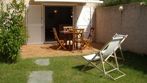 A patio with a table and chairs, a folding chair, and a sliding door leading to a room. - Fully equipped studio in the heart of the vineyard (Patrimonio)