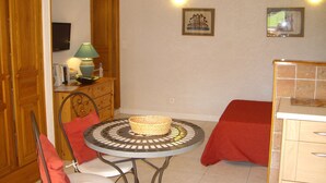 A compact room with a small round table, two chairs, a bed with a red blanket, a wooden cabinet, a television, and two wall-mounted lights. - Fully equipped studio in the heart of the vineyard (Patrimonio)