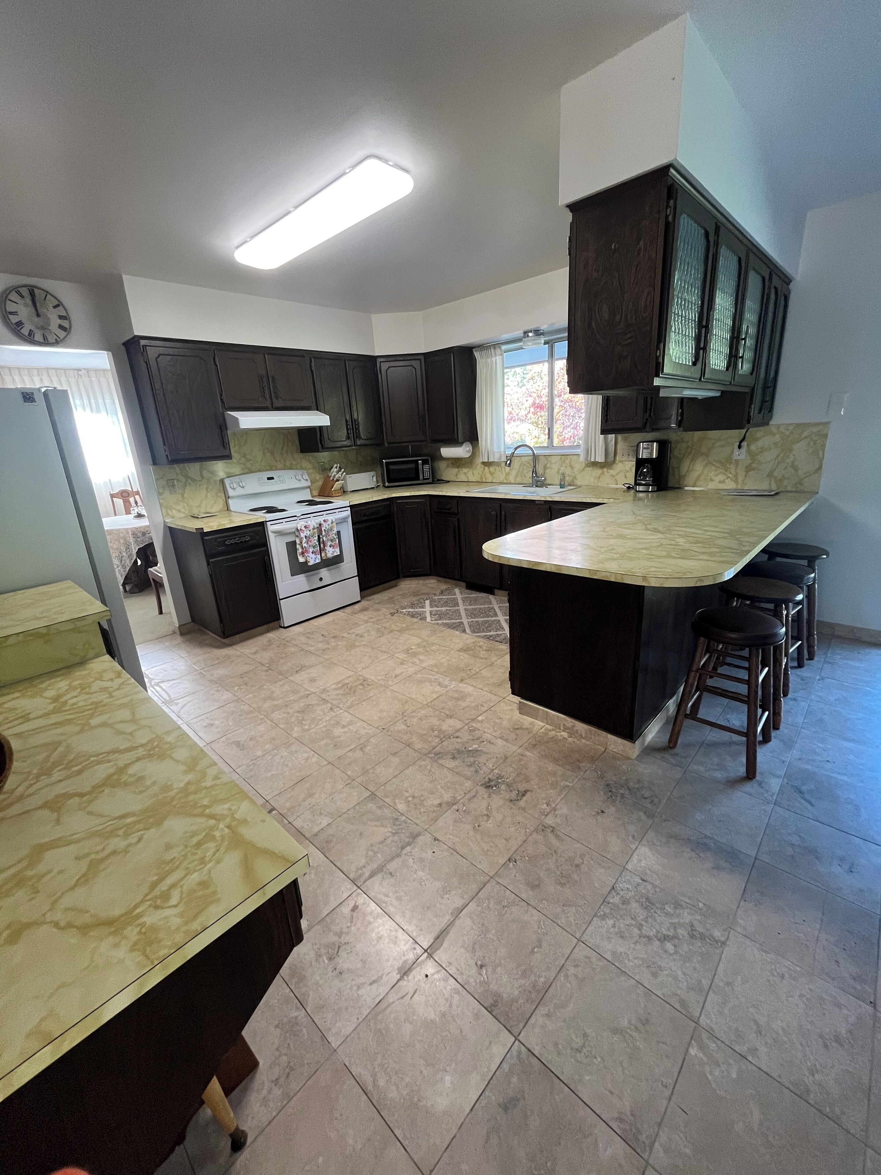 A kitchen with dark cabinets, a white stove, a microwave, and a large island with stools.