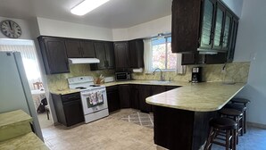 Una cocina con armarios oscuros, una estufa blanca, un microondas y una isla grande con taburetes.