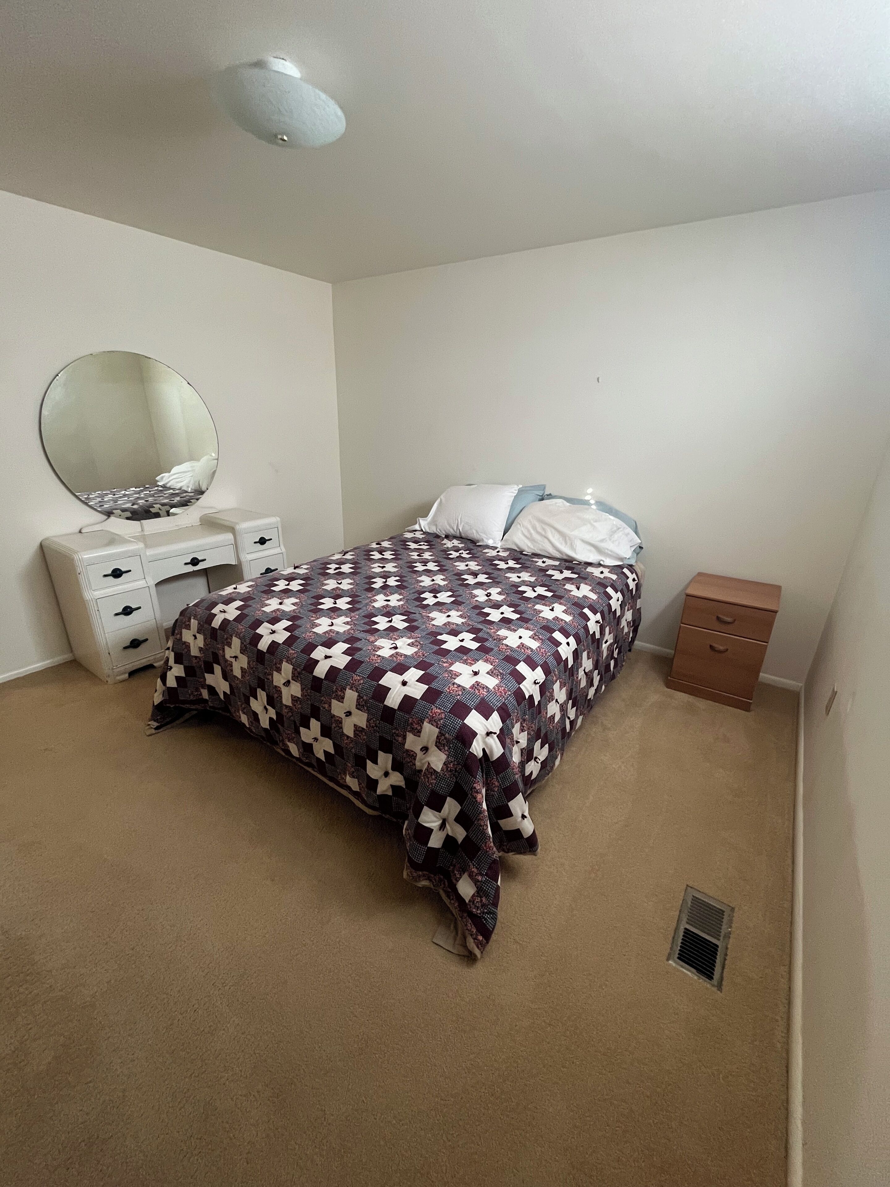 A bedroom with a bed, a dresser, a mirror, and a small cabinet.