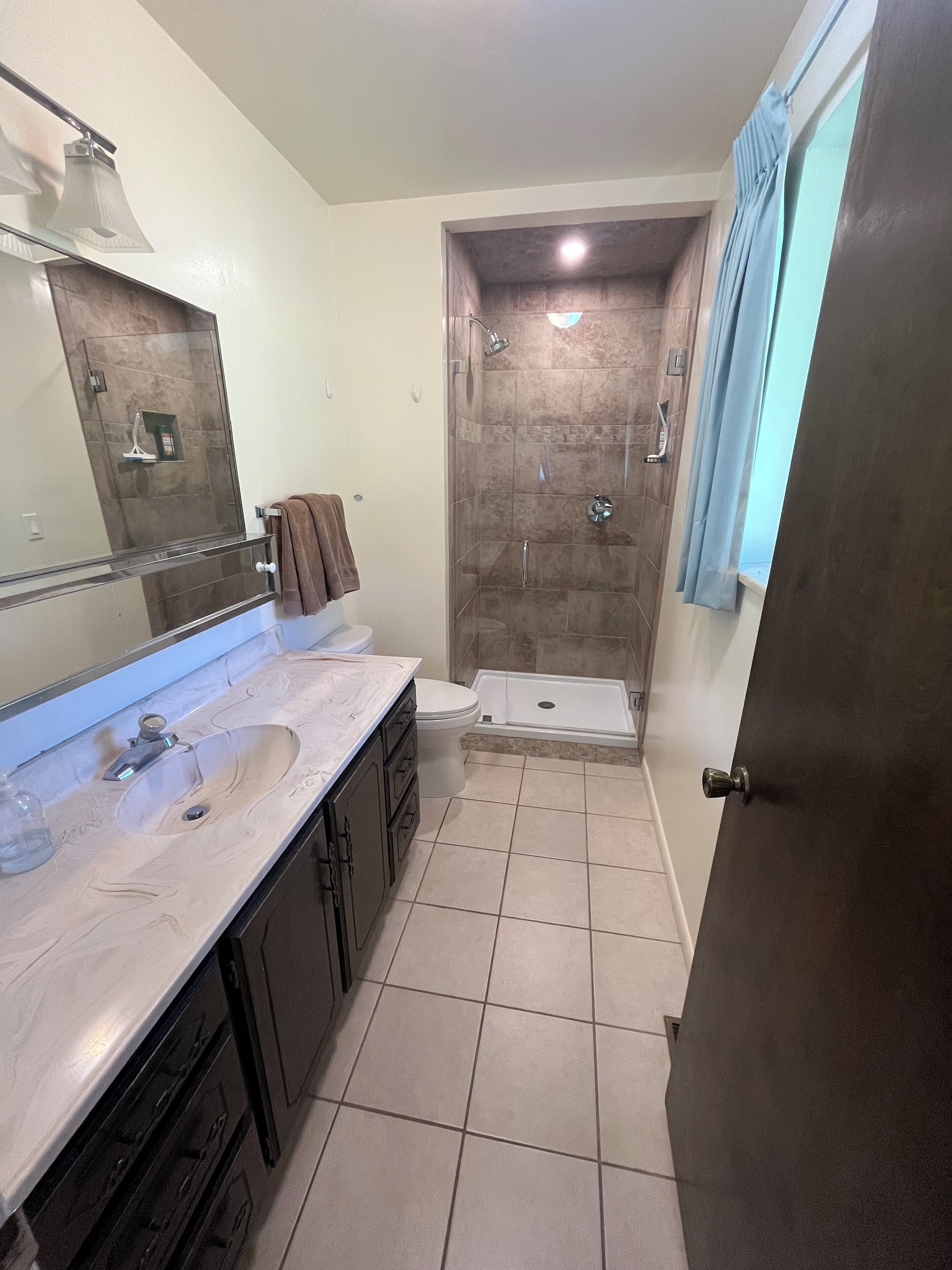 Une salle de bain avec une douche à parois de verre, des toilettes, un lavabo avec un miroir et une serviette accrochée au mur.