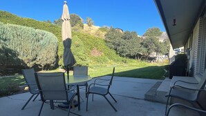 Un patio al aire libre con una mesa y sillas, una sombrilla y vistas a un jardín en una ladera.