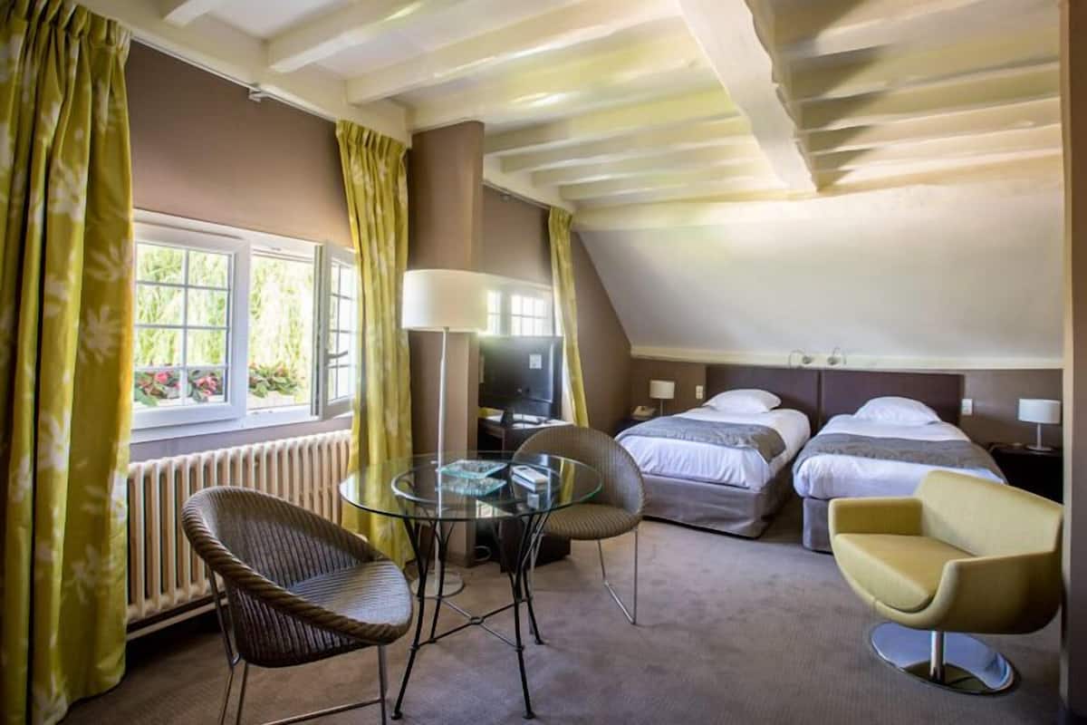 A compact hotel room with a single bed, a sofa, a chair, a glass table, and a TV.