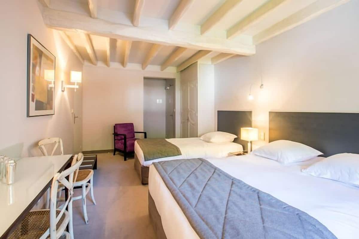A hotel room with two beds, a desk with a chair, a small table, and a purple chair.