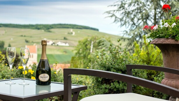 A table with a bottle of Dom Ruart wine and two glasses, overlooking a scenic landscape with rolling hills and a view of a distant village. - Auberge Le Relais (Reuilly-Sauvigny)
