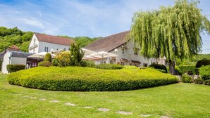 A white building with a red roof, surrounded by well-maintained hedges and a large weeping willow tree. - Auberge Le Relais (Reuilly-Sauvigny)