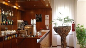 Una zona de bar con mostrador de madera, estantes con botellas, una licuadora y una escultura única con forma de árbol.