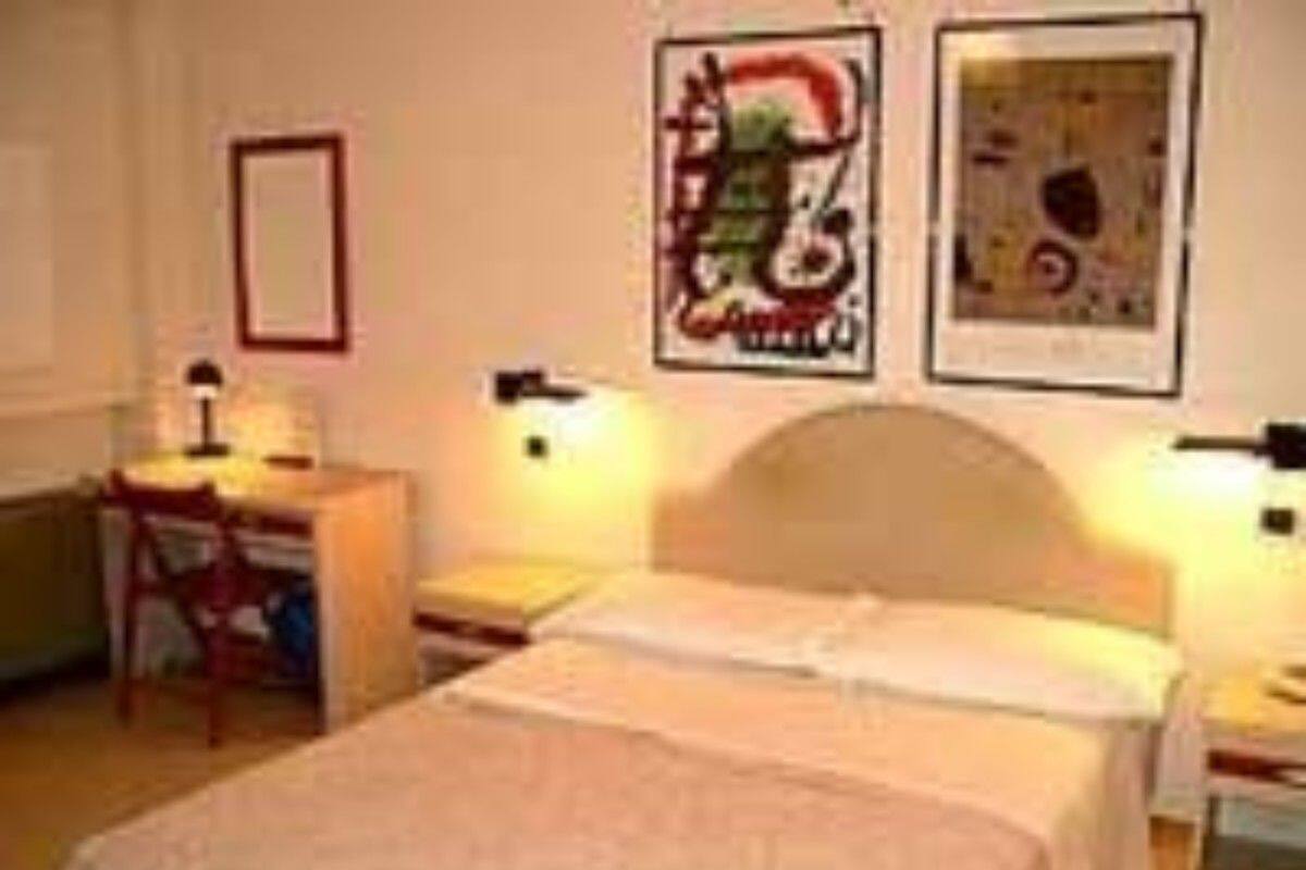 Quarto de hotel com uma cama, uma escrivaninha e duas luminárias de parede.