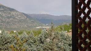 Paisaje montañoso con vista a edificios distantes, rodeado de árboles de hoja perenne.