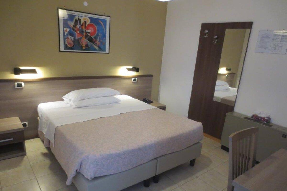 Quarto de hotel com cama, mesas de cabeceira, escrivaninha e uma cadeira.