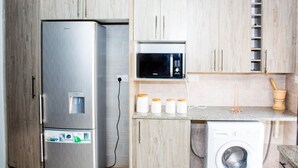 Une cuisine compacte équipée d’un réfrigérateur en acier inoxydable, d’un four à micro-ondes et d’un lave-linge.