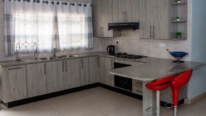 Une cuisine moderne avec des meubles en bois, une cuisinière à gaz, un évier et un tabouret de bar rouge.