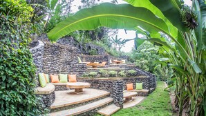 Un patio de piedra con mobiliario exterior y un exuberante jardín de fondo.