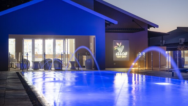 A modern building with a pool area, featuring a sign that reads "aloe - day spa".
