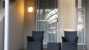 A modern room with two black wicker chairs and a small table, large windows with sheer curtains, and a light fixture on the wall.