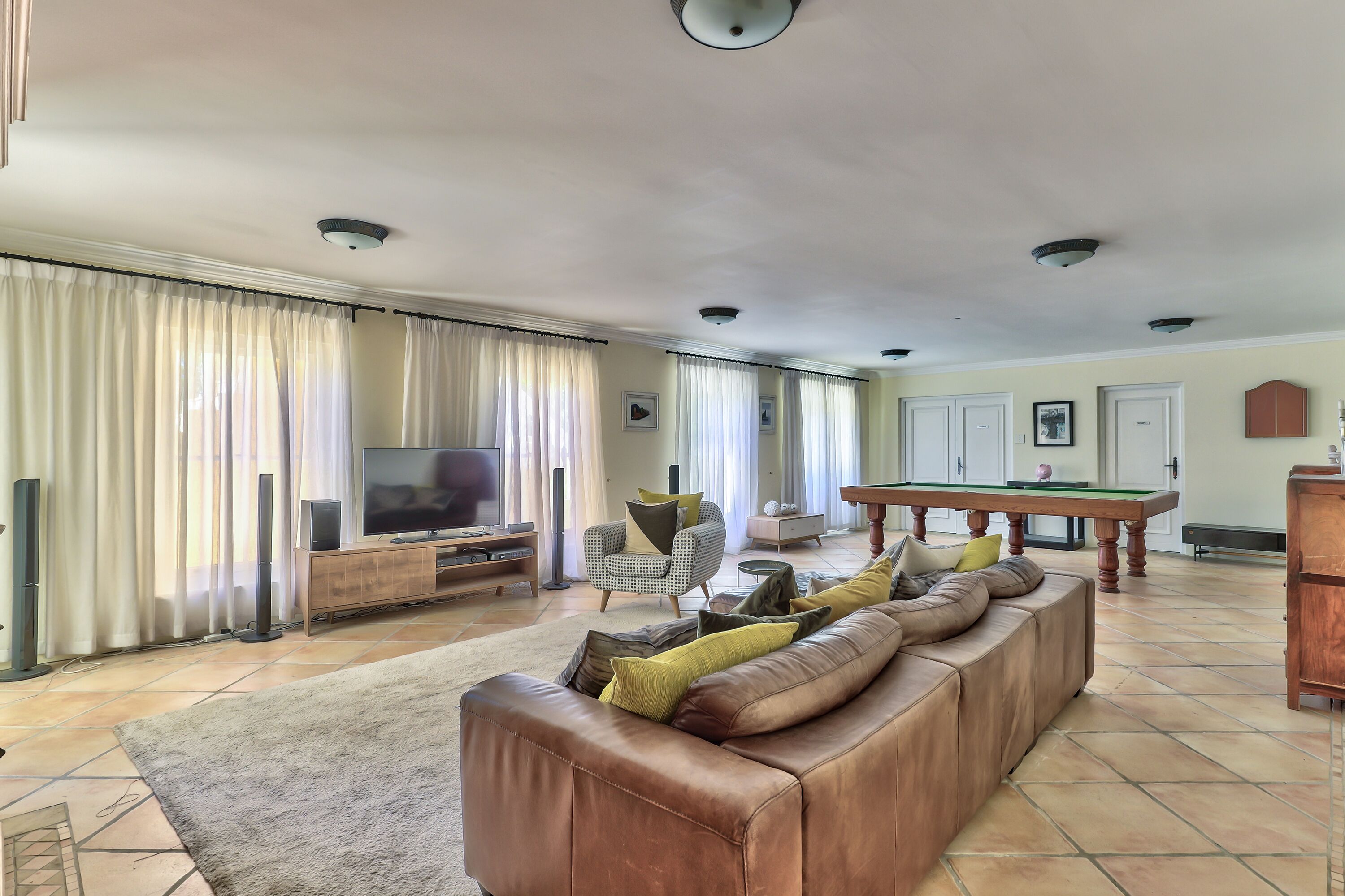 A living room with a leather sofa, a television, a pool table, and a billiards table.