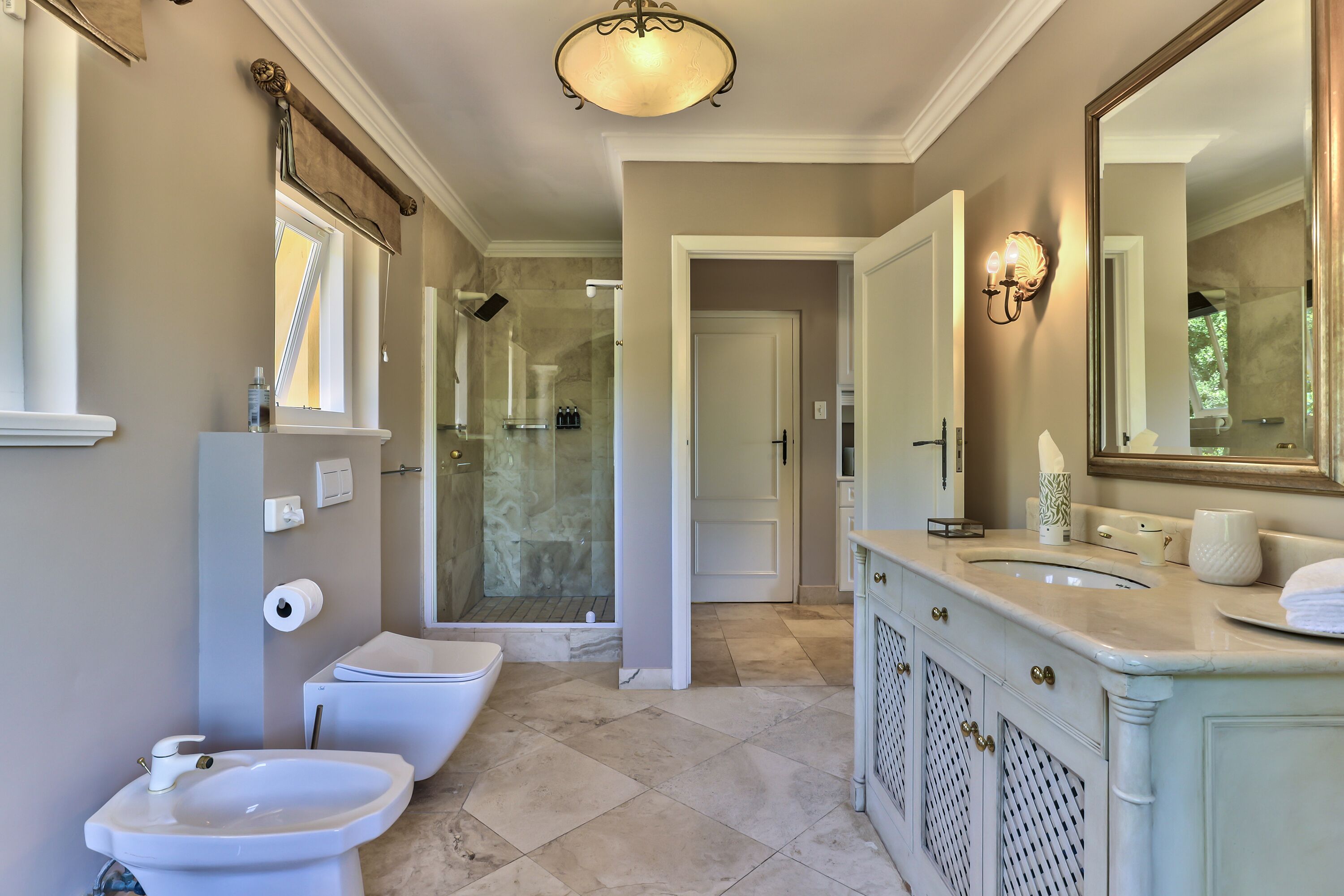 A bathroom with a toilet, bidet, and sink, a shower with glass doors, and a large mirror.