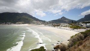 Una playa costera con una orilla arenosa, olas y una montaña al fondo.