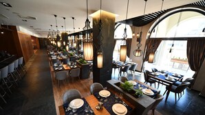 A modern restaurant with long communal tables, individual booths, and hanging pendant lights. - Hotel Austria & Bosna (Sarajevo)