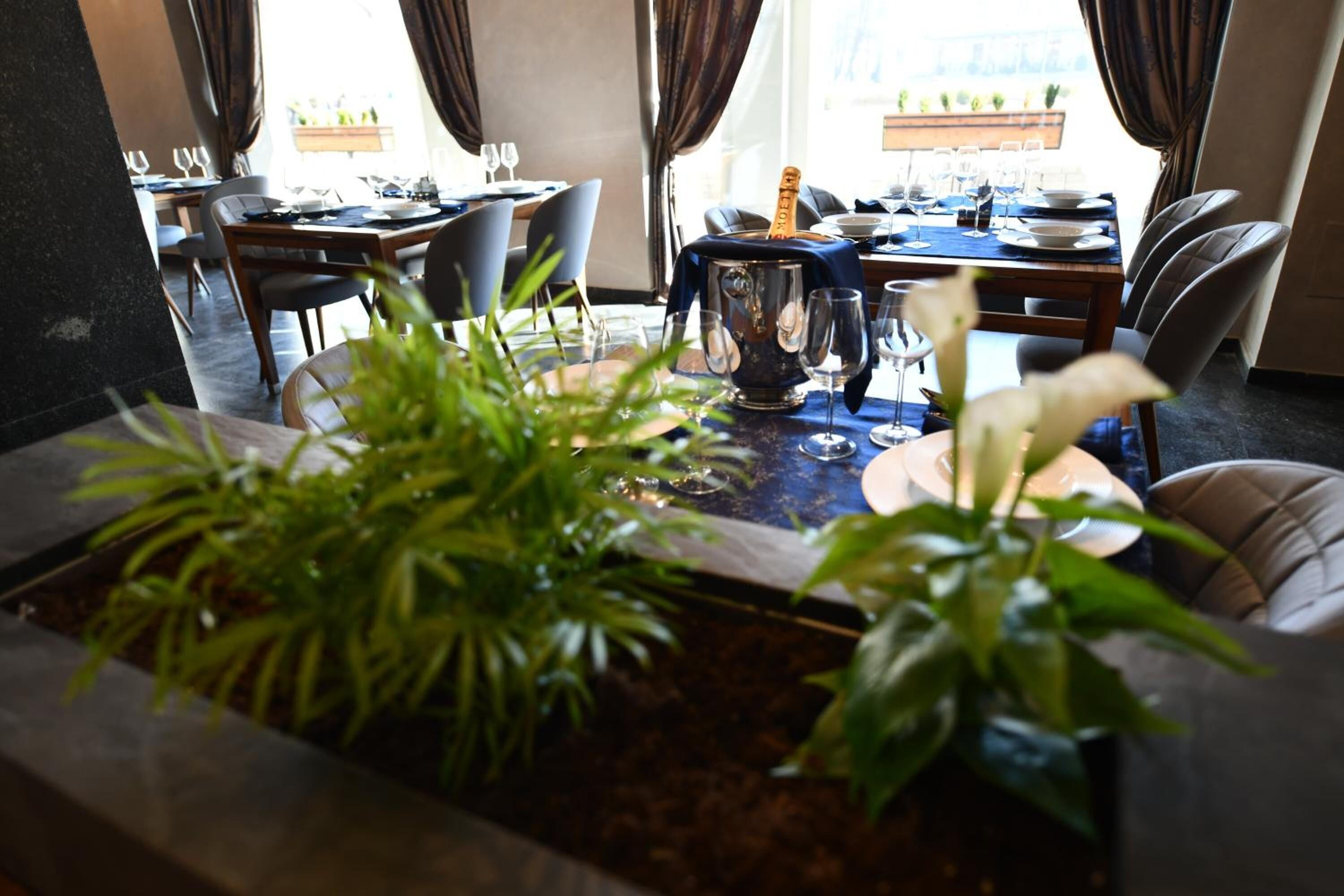 A dining area with tables set for a meal, a large vase with a bottle, and potted plants.