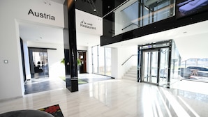 A modern hotel lobby with a glass entrance, a sign reading "Austria," and a staircase leading to an upper level. - Hotel Austria & Bosna (Sarajevo)