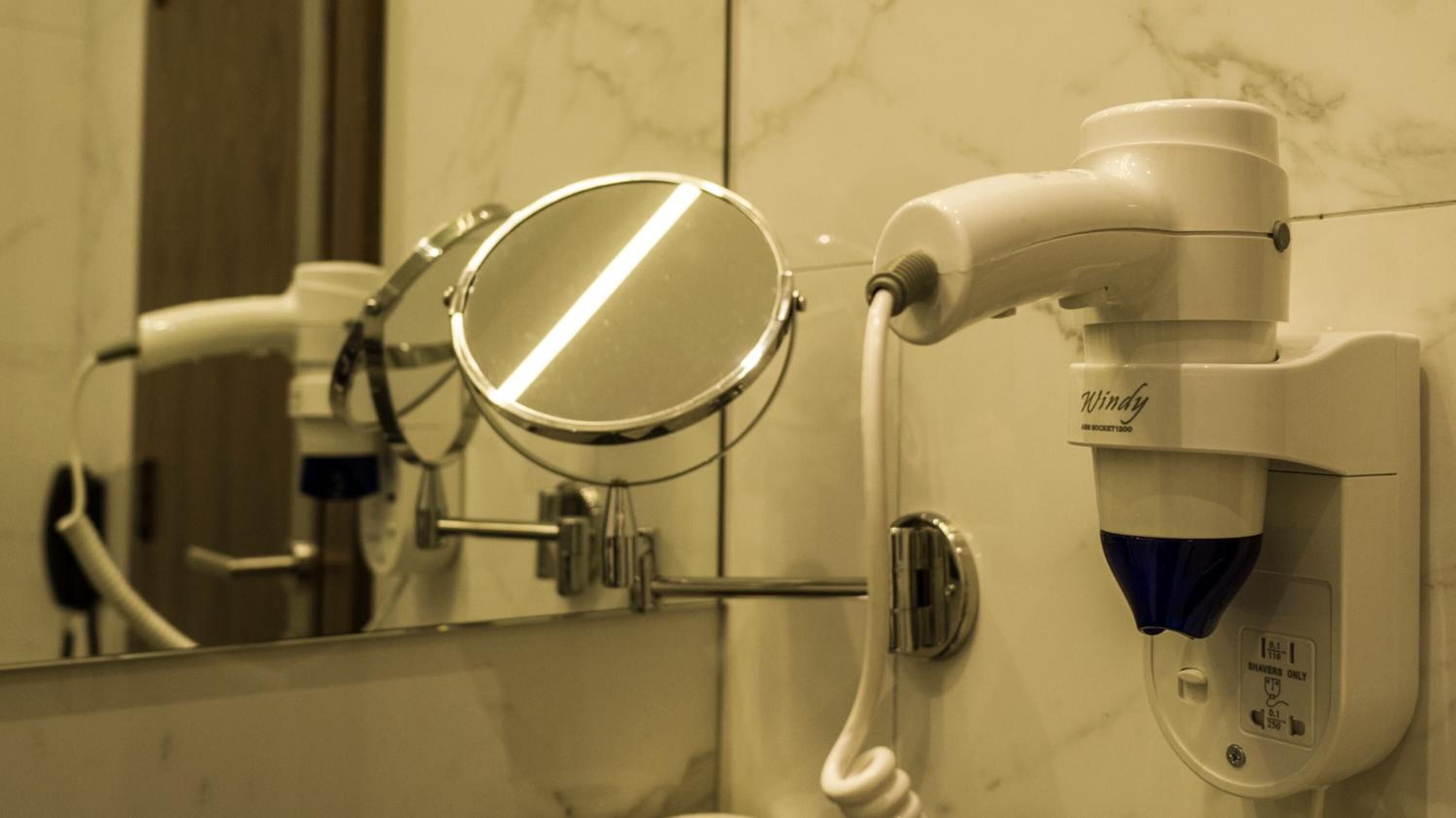 A bathroom with a hand dryer, a mirror, and a towel dispenser.