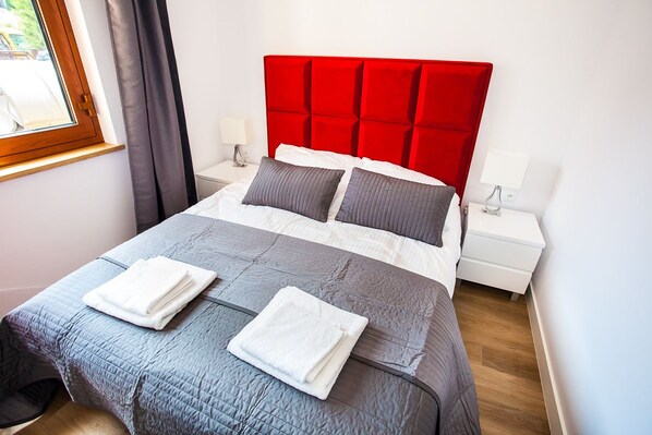 A neatly made bed with a red headboard, grey bedding, and two white towels.