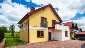 A two-story house with a yellow facade, a red roof, and a brick patio. - Apartamenty SaltApart 2 (Wieliczka)