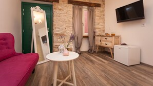 A room with a stone wall, a green door, a pink sofa, a small round table with a vase, a TV on the wall, and a white mini-fridge. - Apartments and Rooms Hey Rovinj (Rovinj)