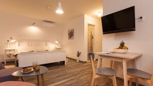 A modern, well-lit living room with a bed, a dining area with a table and chairs, and a mounted TV. - Apartments and Rooms Hey Rovinj (Rovinj)
