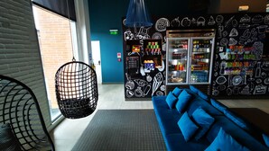 Un interior moderno con sofá azul, una silla colgante, una máquina expendedora y un refrigerador lleno de bebidas.