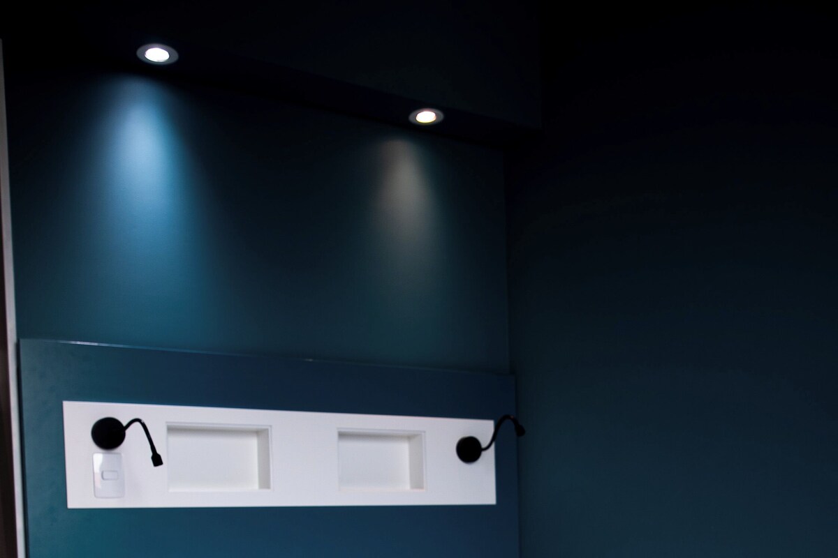 A neatly made bed with white linens in a room with teal walls and recessed lighting.