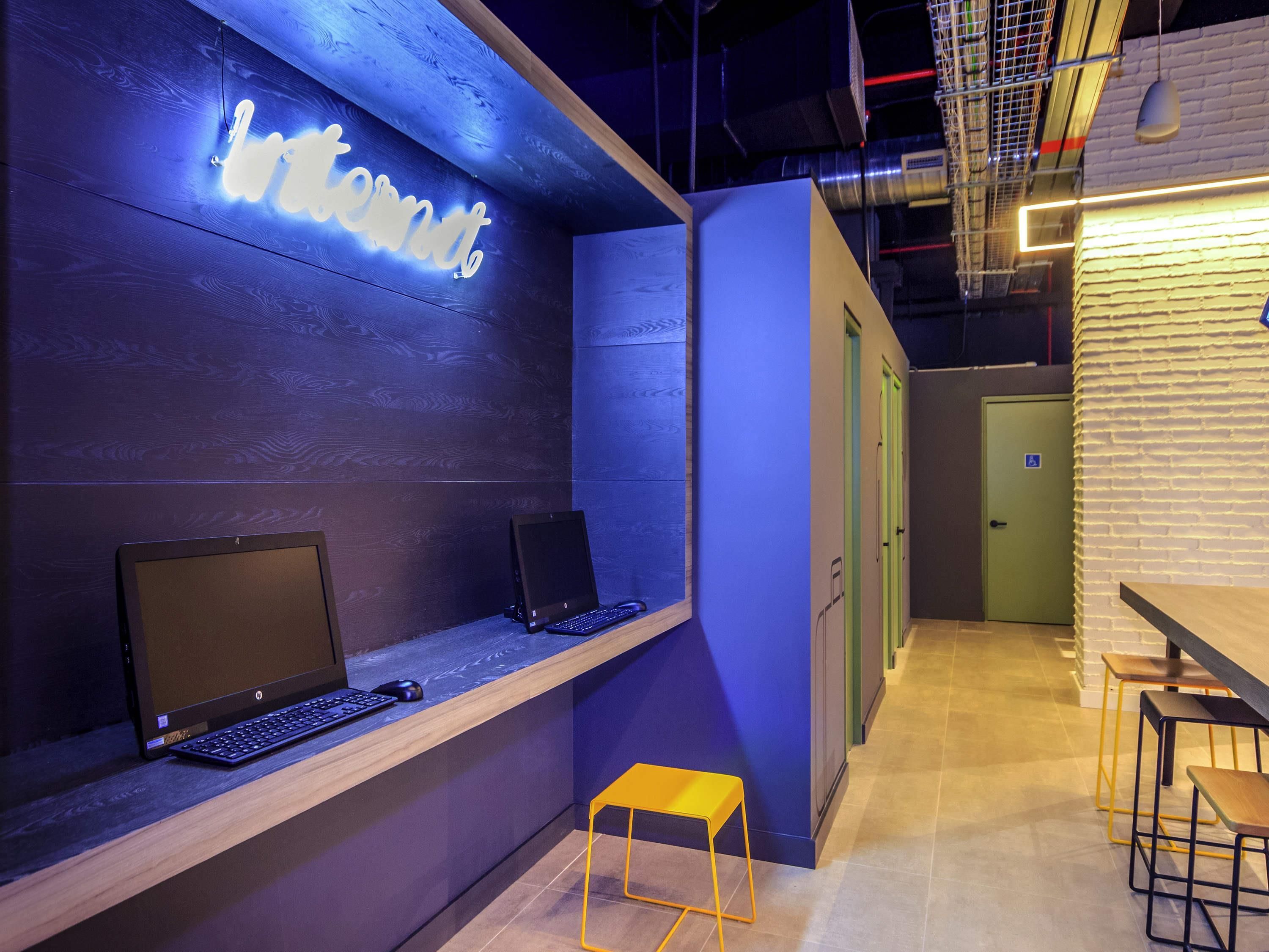 A modern workspace with two HP monitors on a wooden desk, a neon sign reading "Internet," and a yellow stool.