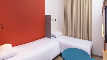 Une chambre d’hôtel avec deux lits simples, une petite table ronde, une télévision et une fenêtre avec des rideaux.