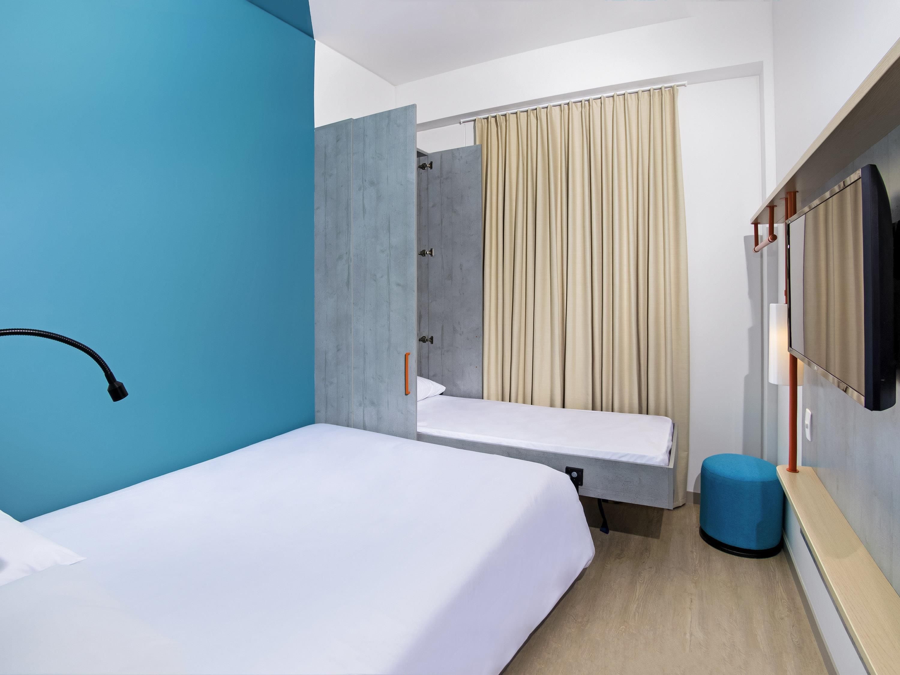 Une chambre d’hôtel comprenant un lit, une petite table, une chaise, un téléviseur et un espace douche.