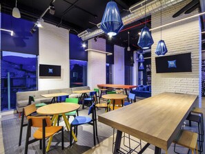 A modern interior with multiple seating areas, including tables and chairs, and a large window providing a view of the outside. - ibis budget Medellín Itagüí Metro (Itagüí)