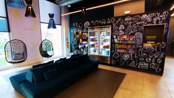 A modern lounge area with hanging chairs, a sofa, a refrigerator stocked with beverages, and a wall decorated with food illustrations.