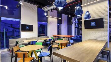 Un intérieur moderne doté de plusieurs espaces de détente, notamment des tables et des chaises, ainsi qu’une grande fenêtre offrant une vue sur l’extérieur.