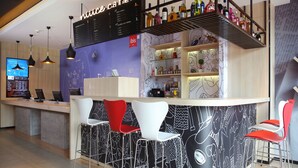 A modern bar area with a menu board, bar stools, and a variety of bottles on shelves. - Ibis Haikou Injoy Plaza Hotel (Haikou)