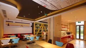 A modern dining area with wooden tables and chairs, a bookshelf, and a counter with a coffee machine. - Ibis Haikou Injoy Plaza Hotel (Haikou)