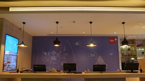 A reception desk with three computer monitors, a digital display, and pendant lighting. - Ibis Haikou Injoy Plaza Hotel (Haikou)