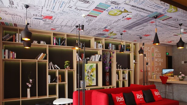 A modern hotel lobby with a red sofa, bookshelves, and a ceiling with sustainability-themed artwork. - Ibis Haikou Injoy Plaza Hotel (Haikou)