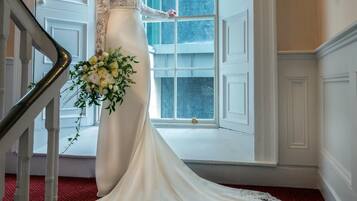 Una novia con un vestido blanco de novia parada frente a una imponente escalera con un amplio ventanal en arco.