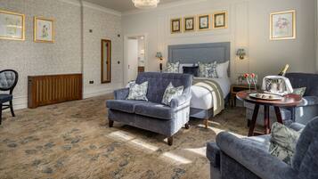 A hotel room with a large bed, two armchairs, a small table with a bottle of champagne, and framed botanical prints on the walls.