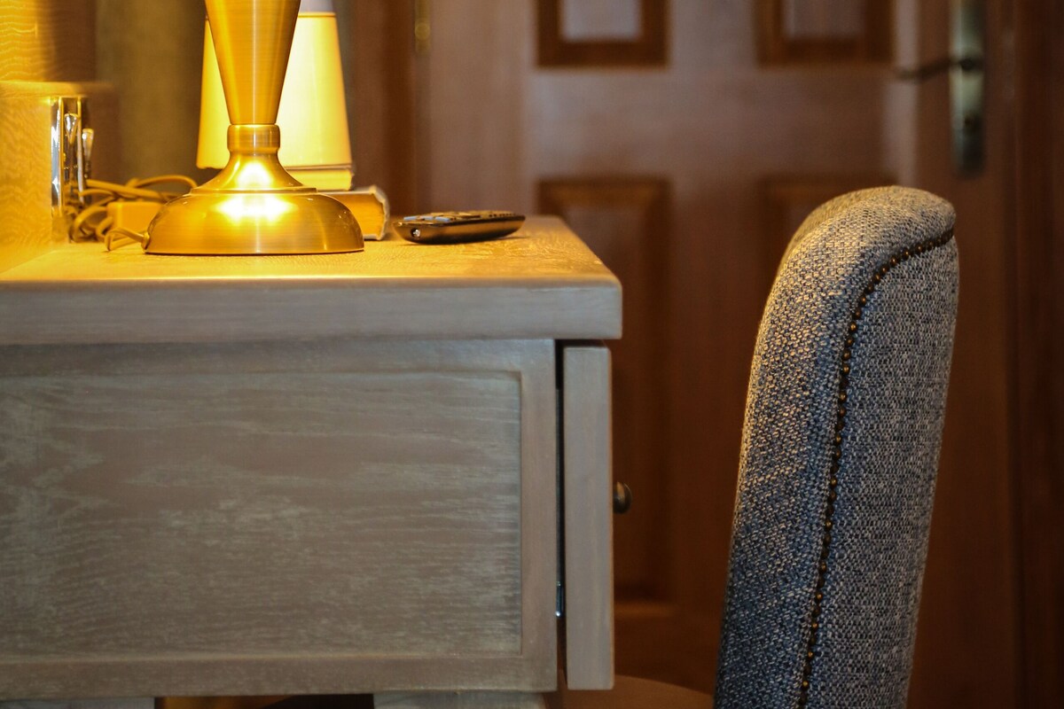 Un escritorio de madera con una lámpara, un control remoto y una silla.