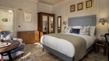 A hotel room with a large bed, a wooden cabinet, a round table with a bottle, and a chair.