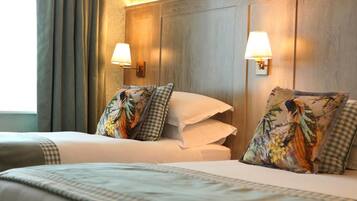 A hotel room with two beds, each with a checkered pillow and a floral pillow. There are two wall-mounted lamps on either side of the beds.